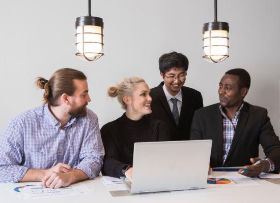 four business students conversing while viewing a laptop